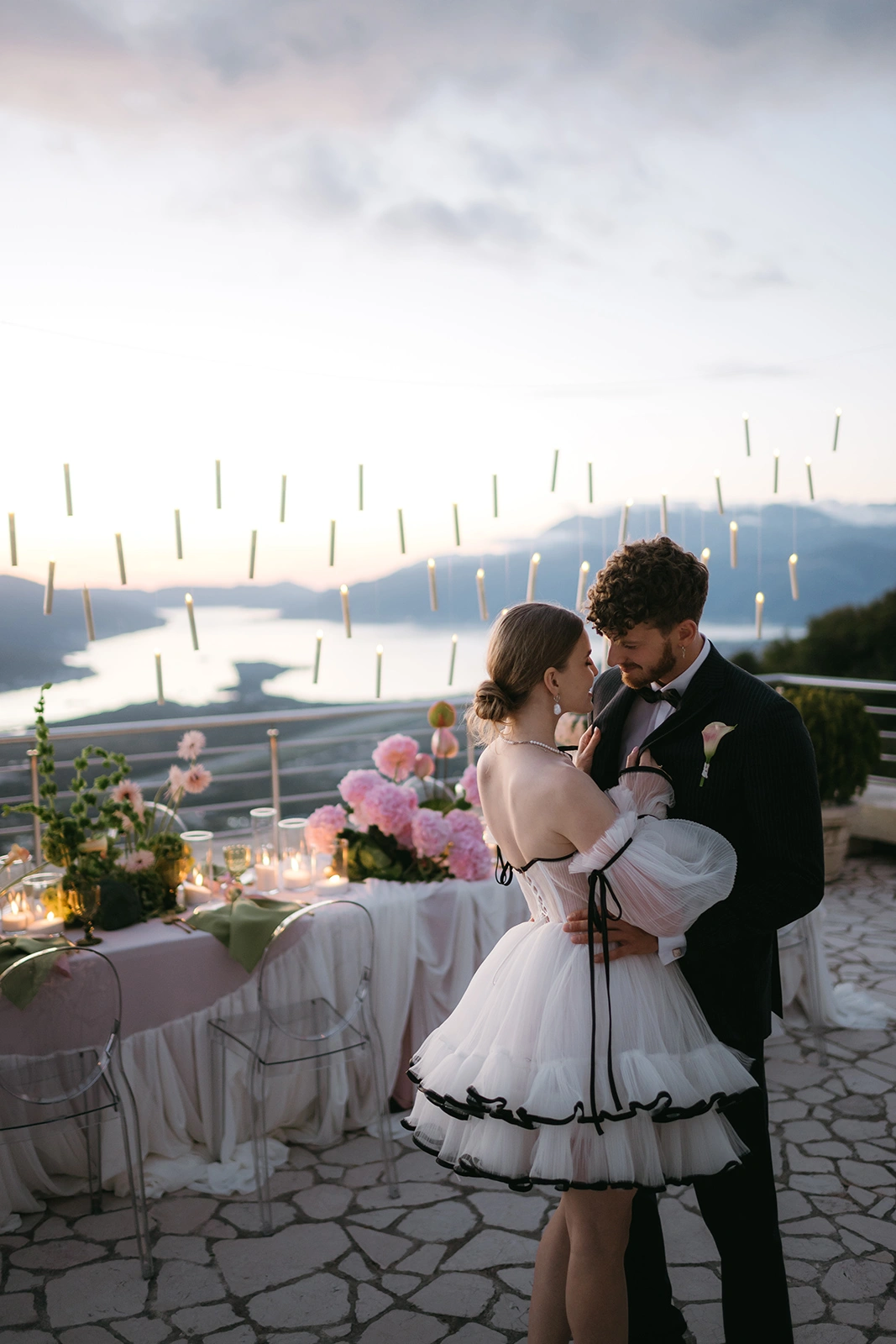 Flottie The Cabbage Affair wedding decor and organisation: bride and groom sharing a tender kiss at twilight beneath a suspended canopy of floating candles against an evening sky