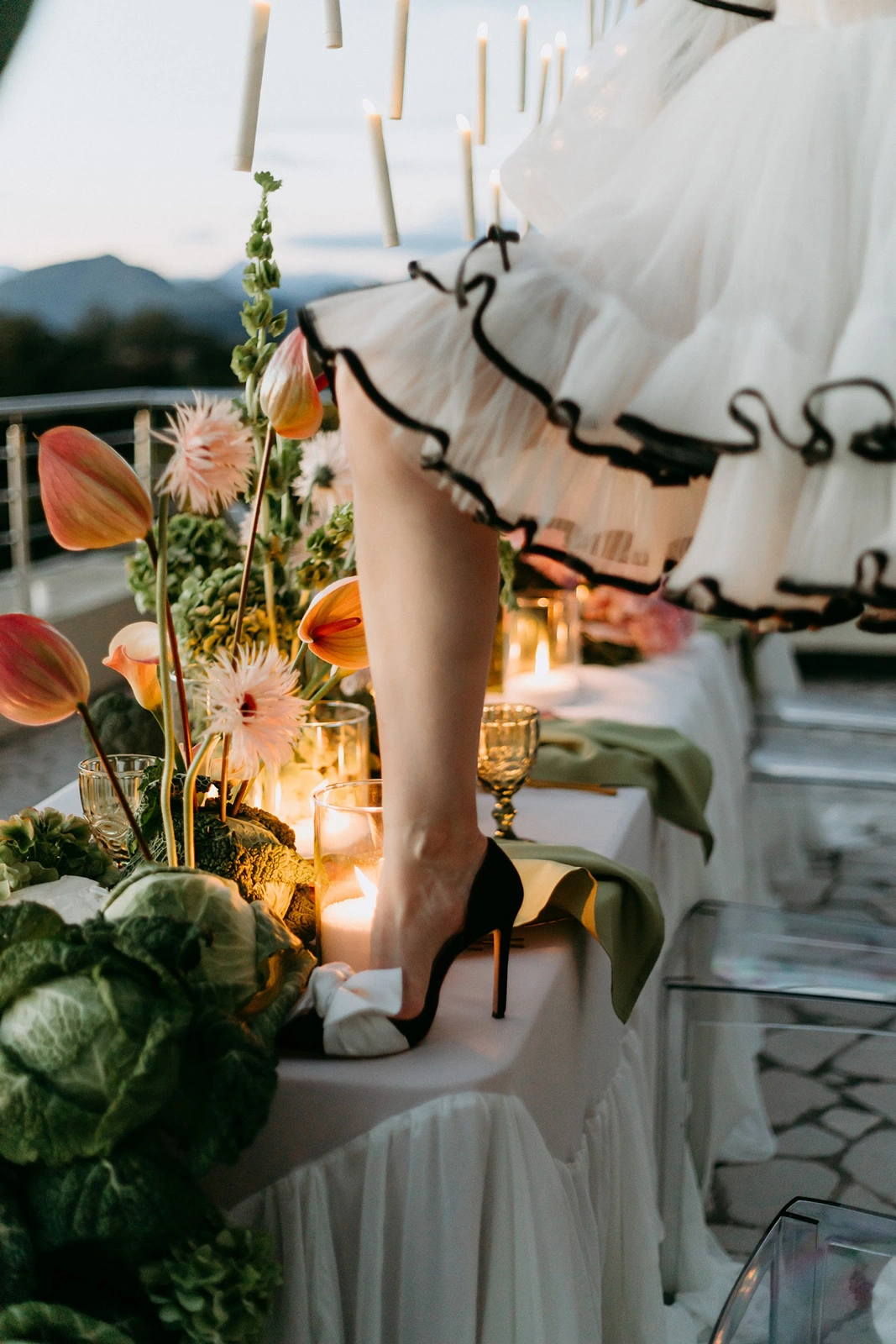 Flottie wedding decor and organisation: close-up shot of a bride in black heels standing by a reception table decorated with fresh cabbage, exotic flowers, and candles