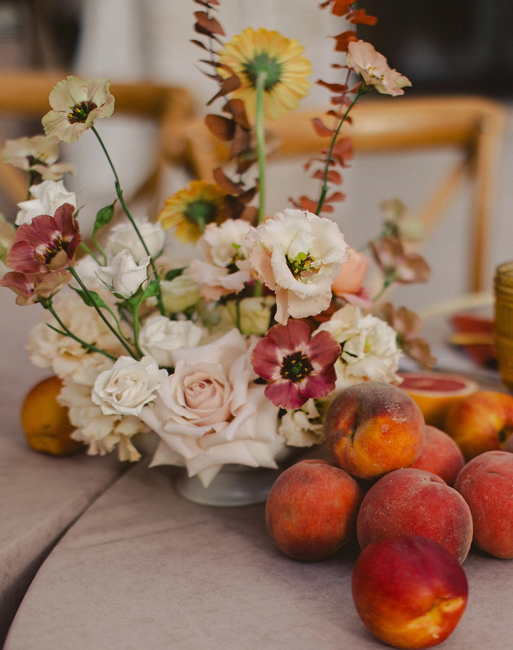 Flottie Peach Haze wedding decor and organisation: close-up of a delicate floral centerpiece arrangement with pastel roses and fresh peaches on a table