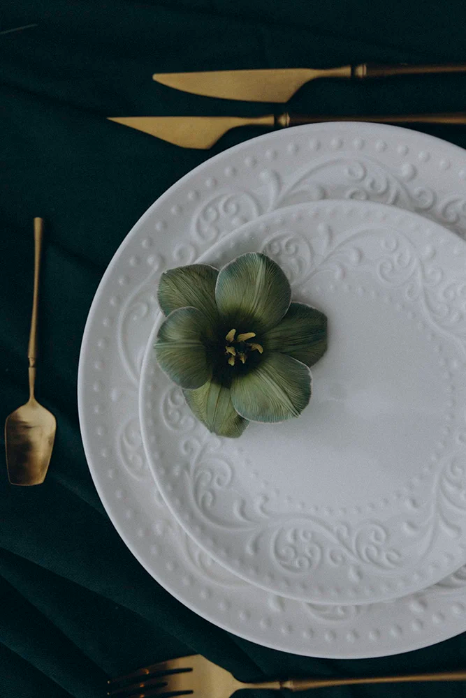 Flottie flower decor, wedding, and organisation at Borgo Lapis in Croatia: elegant table settings featuring embossed white plates, gold cutlery, and a unique green flower detail