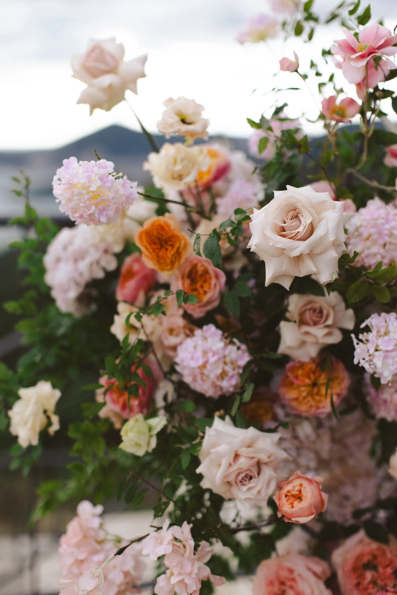 Flottie Peach Haze wedding decor and organisation: lush peach and pink floral arrangement column set against a scenic outdoor coastal background