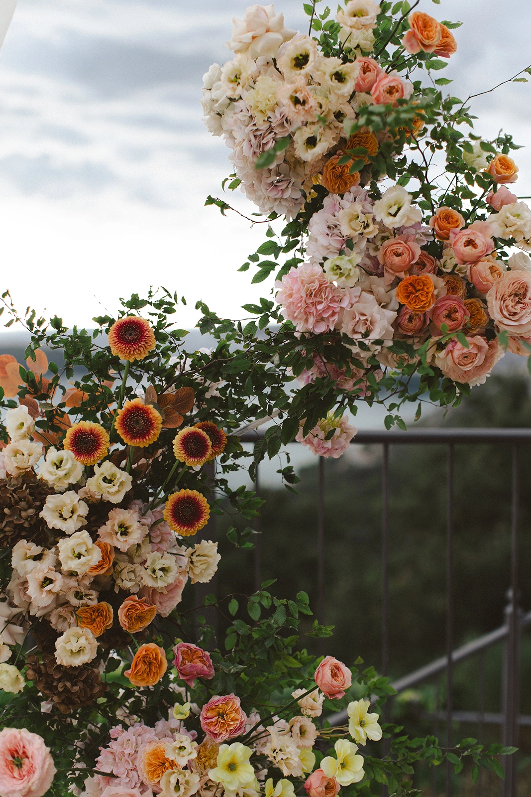 Flottie Peach Haze wedding decor and organisation: lush peach and pink floral arrangement column set against a scenic outdoor coastal background