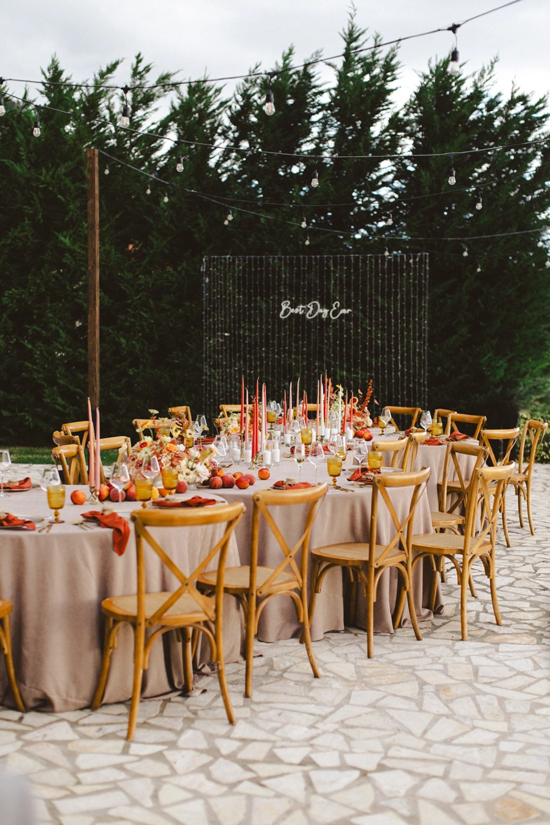 Flottie Peach Haze wedding decor and organisation: aerial view of guests enjoying an outdoor wedding reception dinner at round tables styled with peach-toned florals and candles