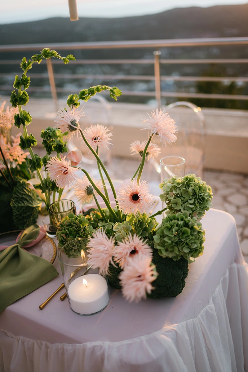 Flottie The Cabbage Affair wedding decor and organisation: close-up of an upscale reception table center-piece featuring fresh heads of cabbage, pastel anthuriums, gerberas, and glowing candles in glass cylinders