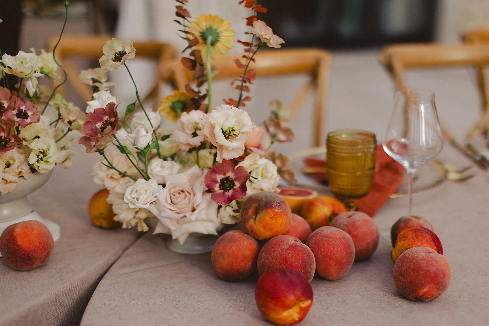 Flottie Peach Haze wedding decor and organisation: close-up of a delicate floral centerpiece arrangement with pastel roses and fresh peaches on a table
