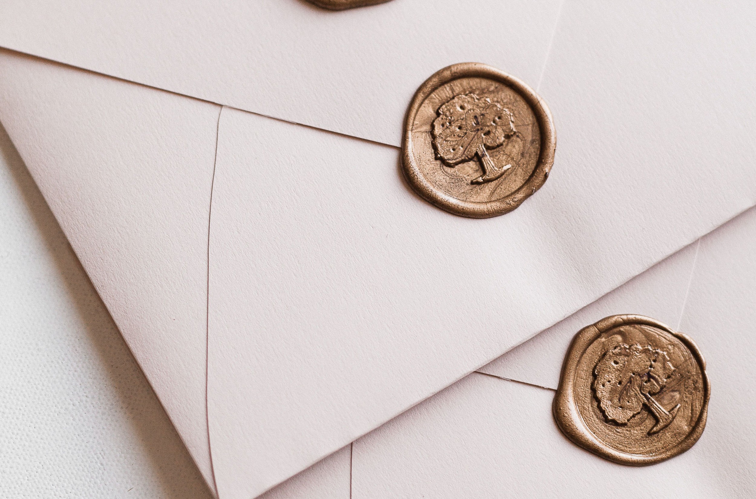 Flottie wedding decor and organisation: close-up of luxury white wedding stationery envelopes sealed with elegant gold wax stamps featuring a bespoke tree motif