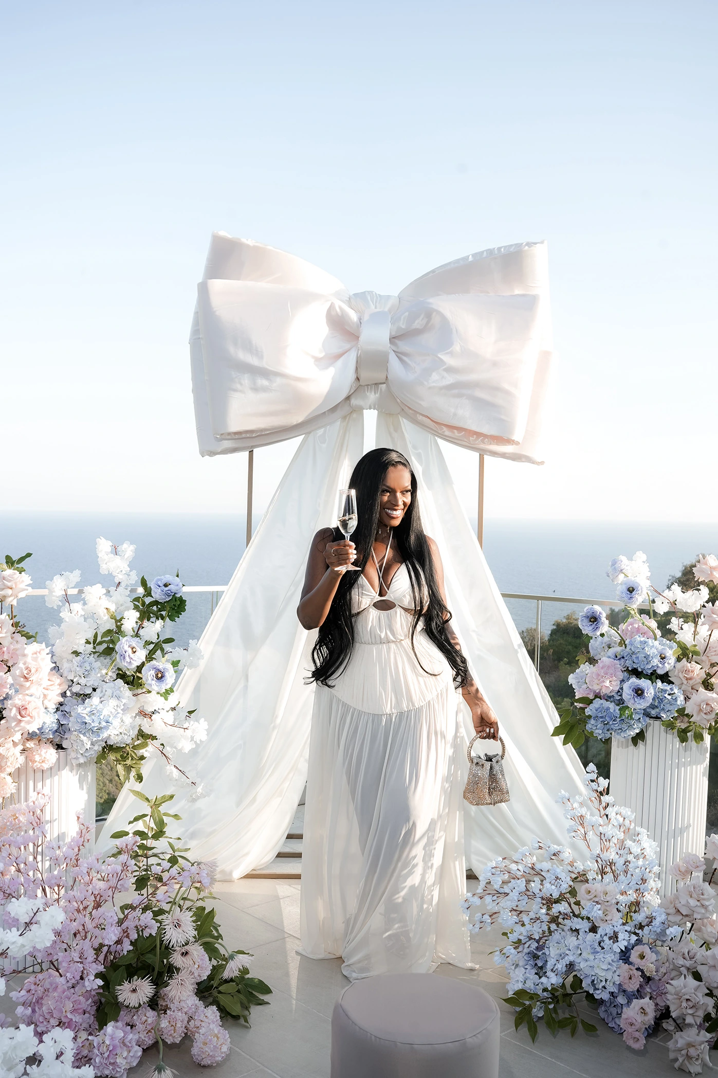 Flottie flower decor, wedding, and organisation at Cape Montenegro in Krimovica: guest holding champagne amid luxury floral arrangements and a large white bow installation