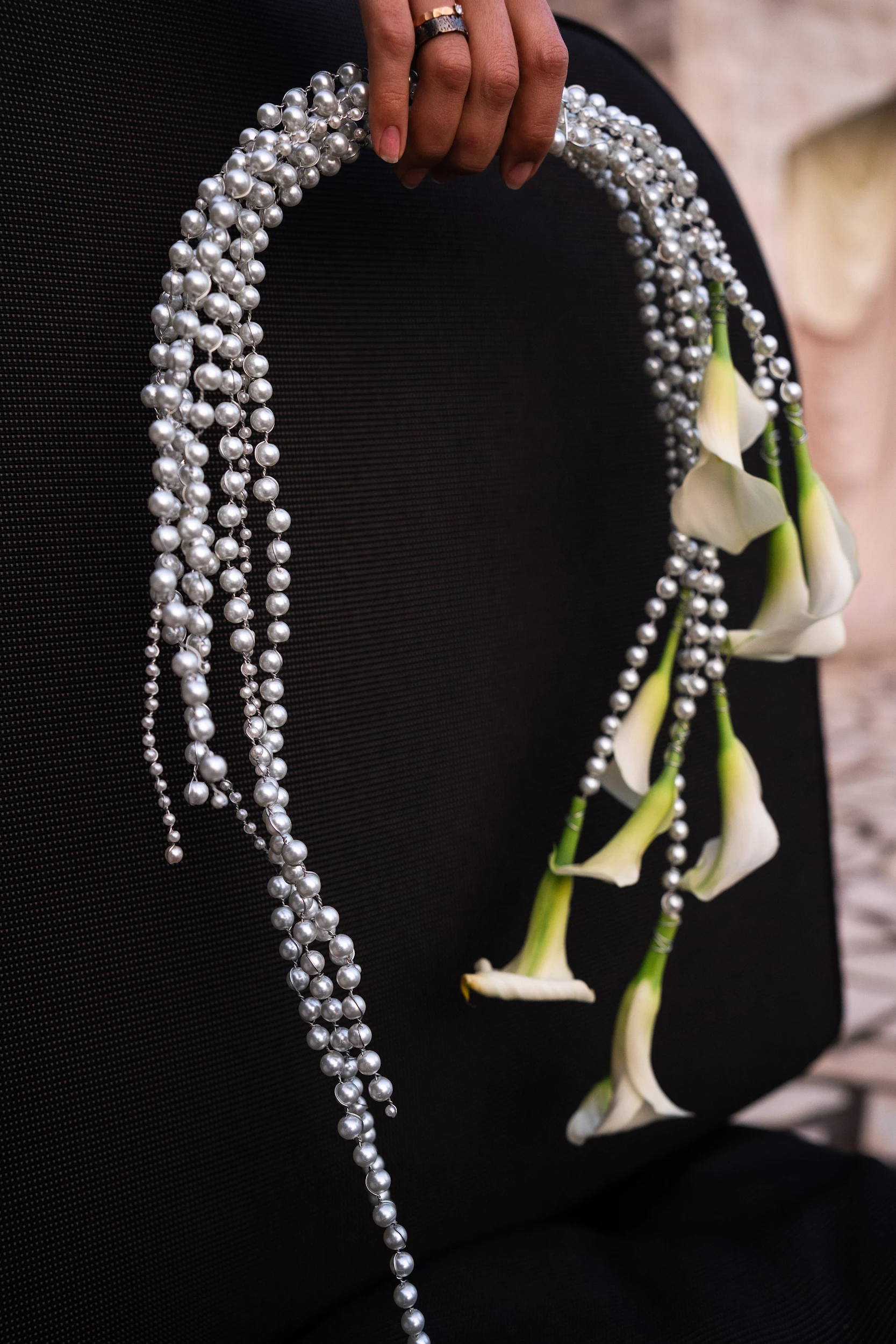 Flottie Shades of Burgundy wedding decor and organisation: close-up portrait of a bride in a satin gown posing behind a cascading curtain of pearls while holding a custom floral arrangement