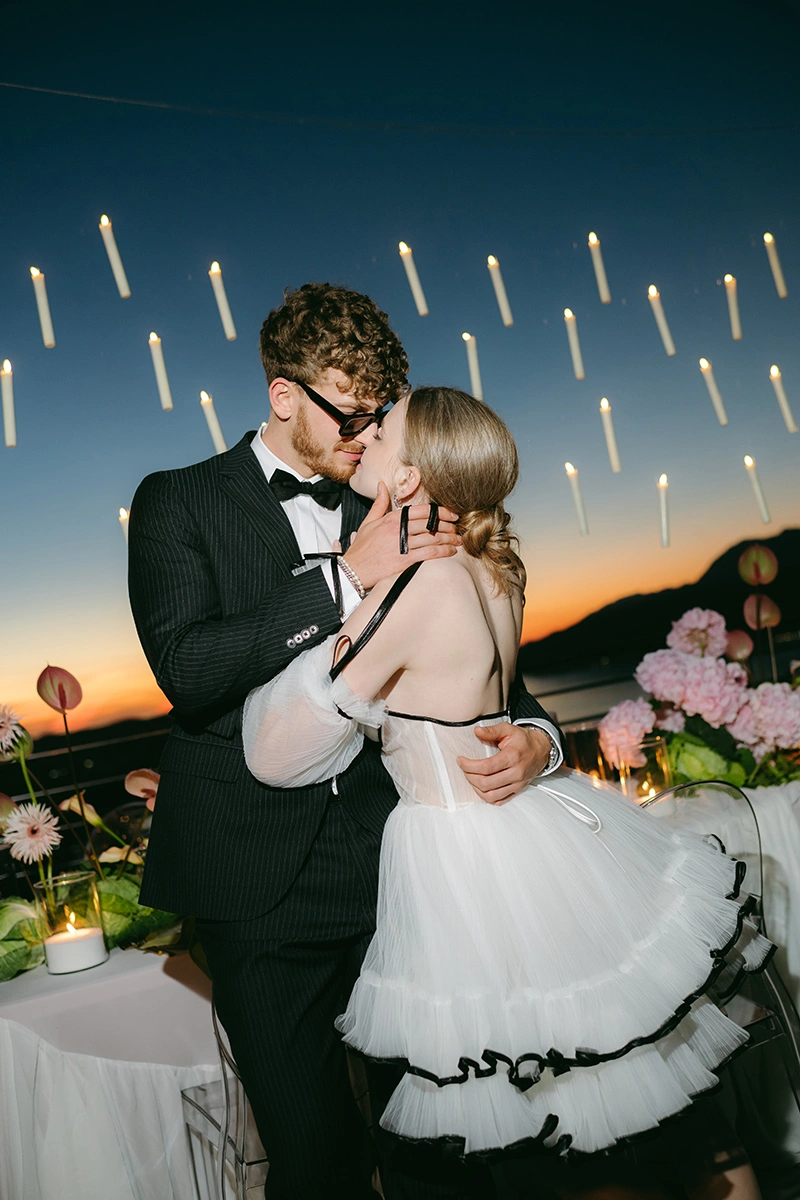 Flottie The Cabbage Affair wedding decor and organisation: bride and groom sharing a tender kiss at twilight beneath a suspended canopy of floating candles against an evening sky