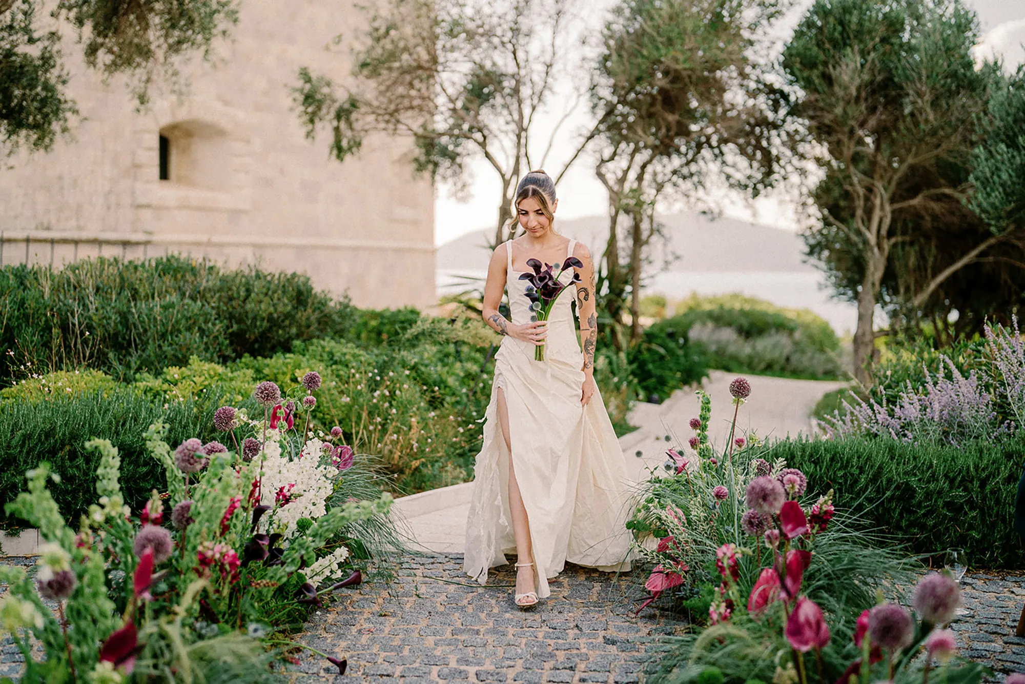 Bride in silk dress walking Mamula Island fortress Montenegro, moody floral bouquet