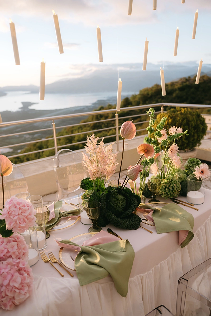 Flottie The Cabbage Affair wedding decor and organisation: close-up of an upscale reception table center-piece featuring fresh heads of cabbage, pastel anthuriums, gerberas, and glowing candles in glass cylinders