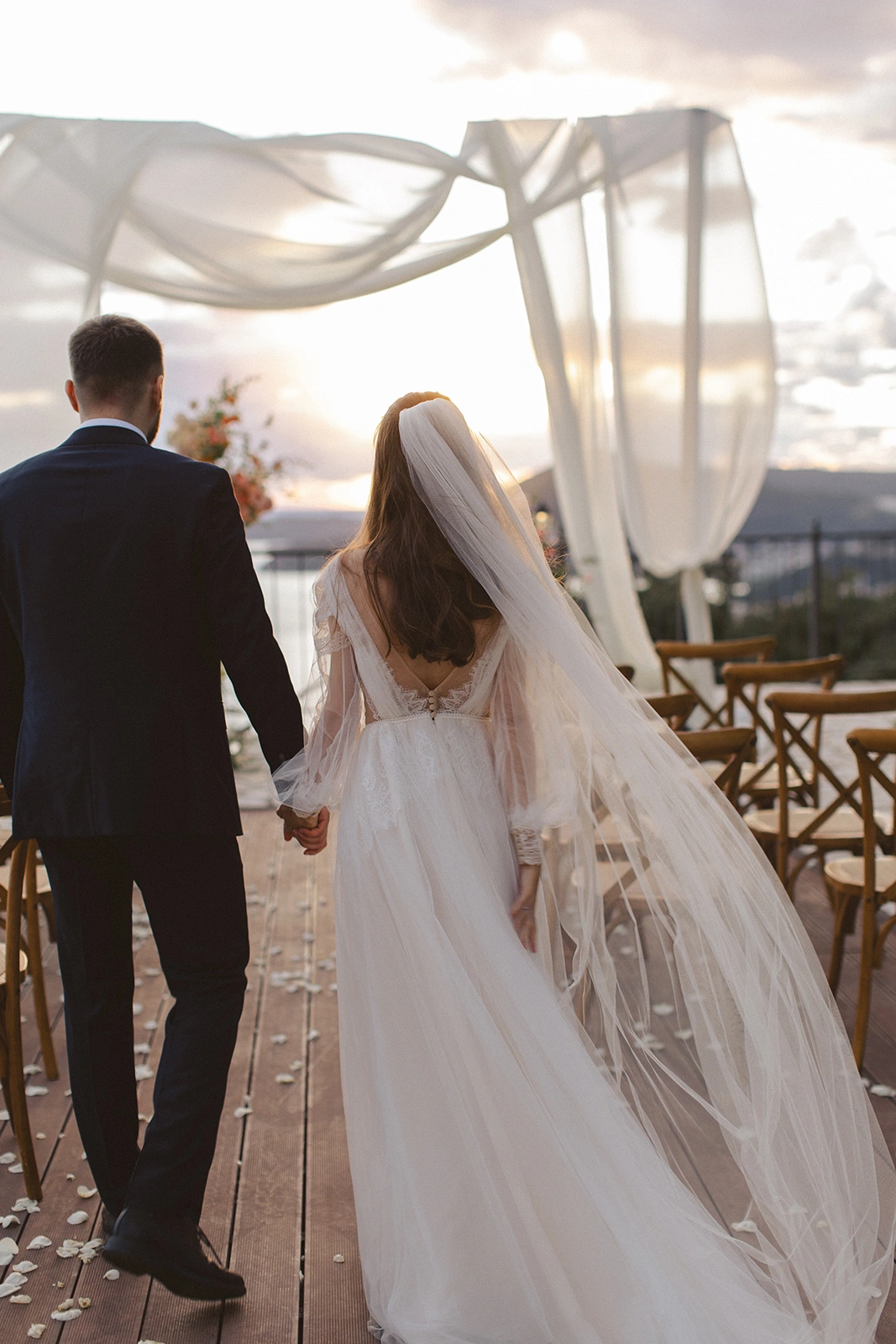 Flottie Peach Haze wedding decor and organisation: bride and groom posing together under a draped archway framed by vibrant peach and pink floral arrangements