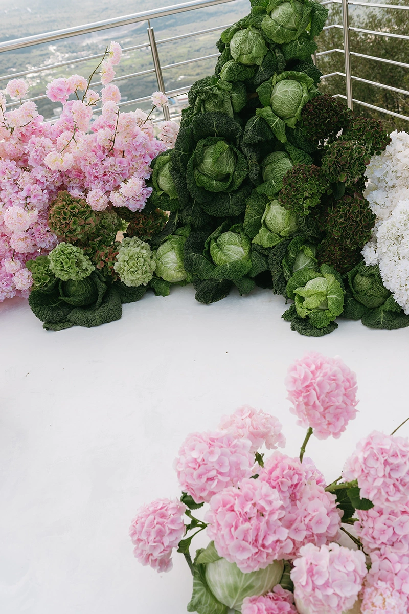 Flottie The Cabbage Affair wedding decor and organisation: modern ceremony setup featuring transparent ghost chairs and a unique sculptural altar installation made of fresh cabbages and pink and white florals overlooking a mountain view