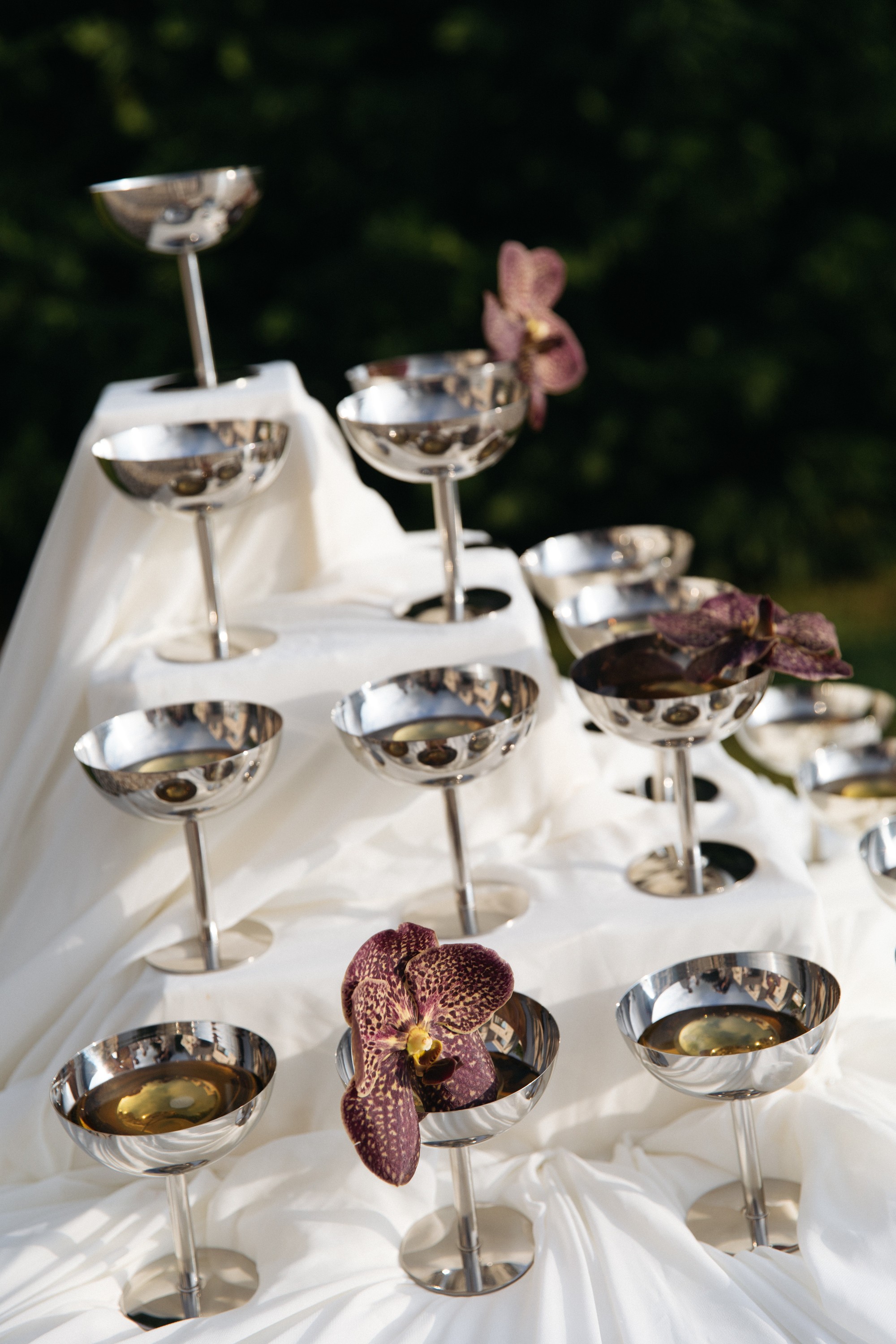 Flottie Shades of Burgundy wedding decor and organisation: bride in a minimalist white gown and groom in a white double-breasted jacket toasting with champagne in front of a draped arch