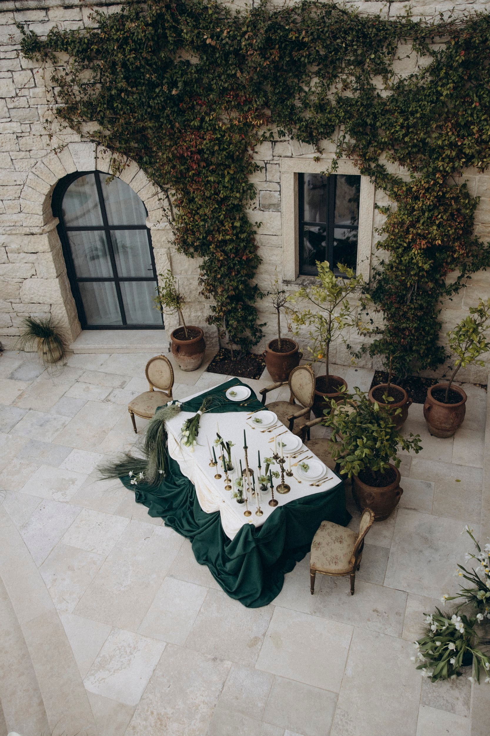 Flottie flower decor, wedding, and organisation at Borgo Lapis in Croatia: aerial view of an open-air courtyard banquet table styled with emerald green textiles, candles, and bespoke floral arrangements